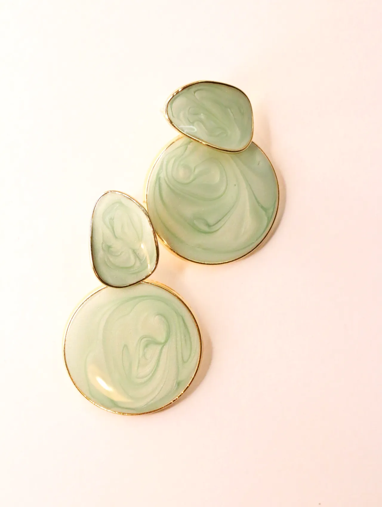 Pareja de pendientes colgantes geométricos con efecto mármol verde menta sobre fondo rosa claro — pendientes dorados, primer plano · Lola y Sol (EAR-075)