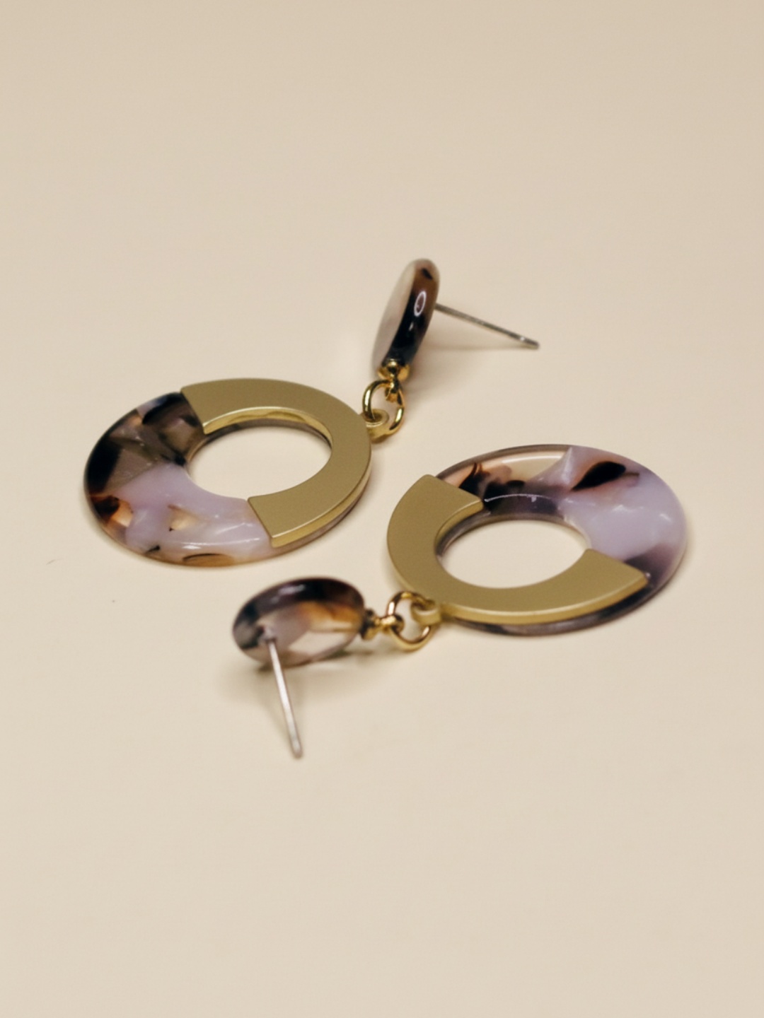 Pendientes dorados marmoleados con pasadores visibles sobre fondo beige — pendientes dorados, primer plano · Lola y Sol (EAR-082)