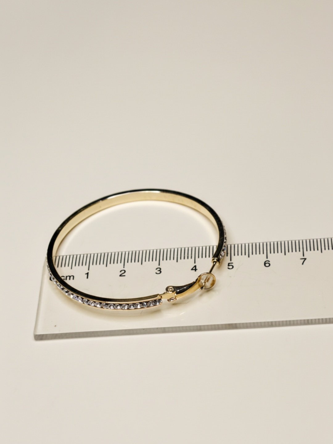 Pendiente de aro dorado con strass junto a una regla — pendientes dorados, primer plano · Lola y Sol (EAR-086)