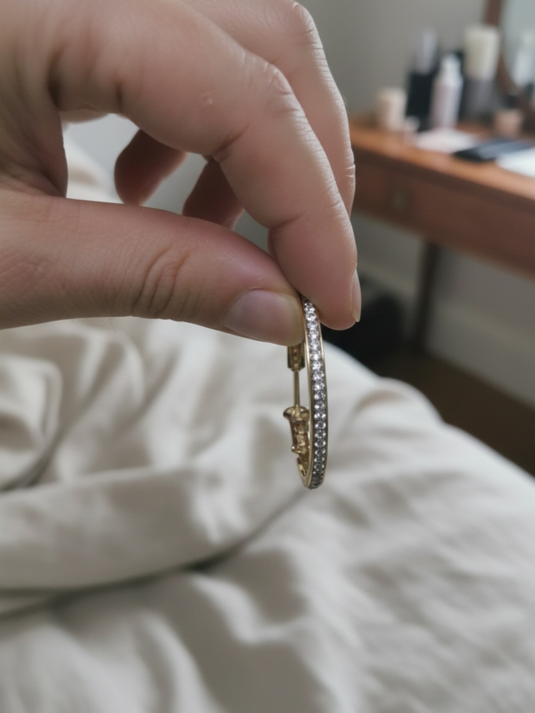 Vista lateral de un pendiente de aro dorado con strass sostenido con la mano — pendientes para mujer, vista principal · Lola y Sol (EAR-087)