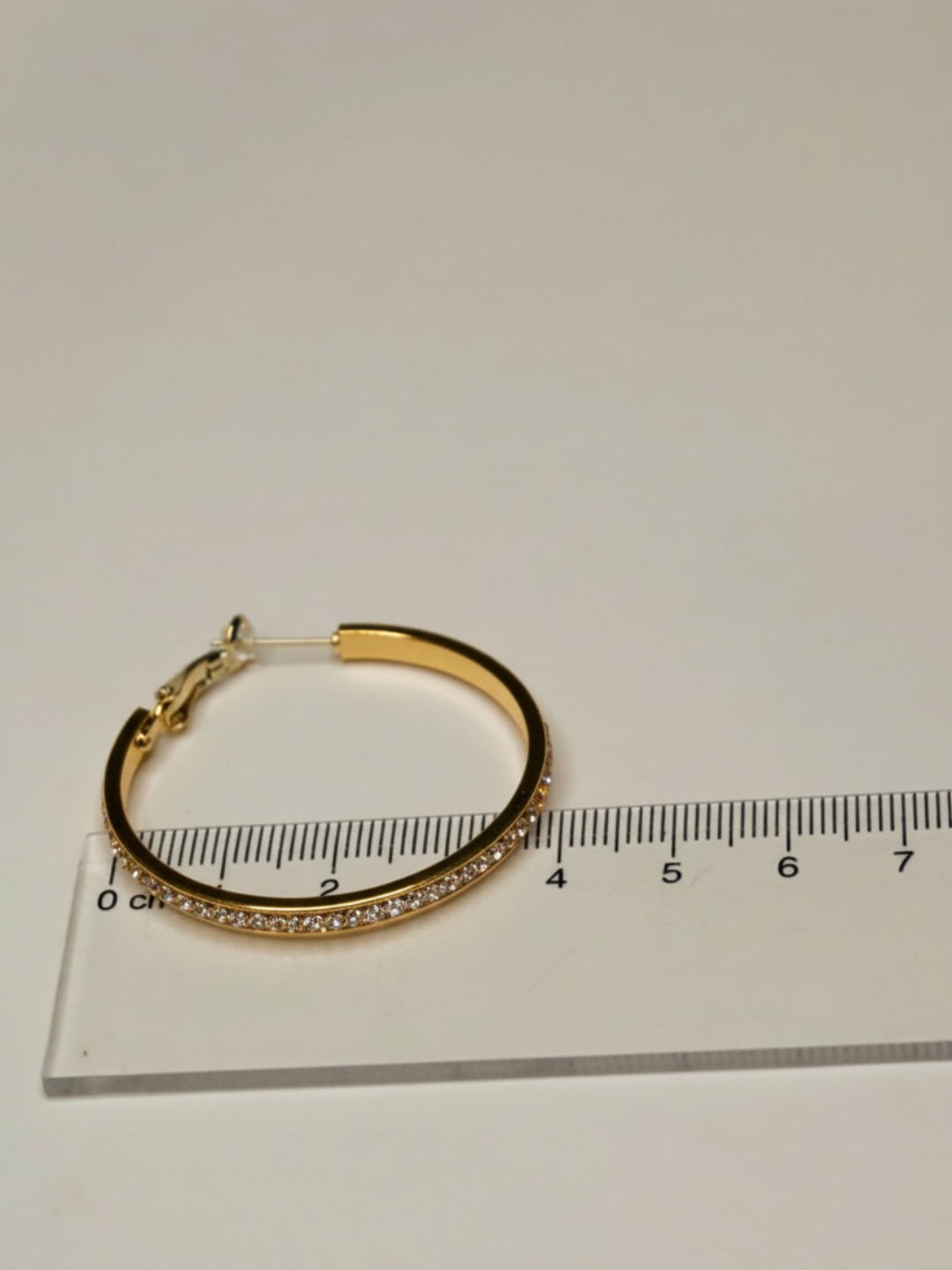 Pendiente de aro dorado con strass junto a una regla — pendientes dorados, primer plano · Lola y Sol (EAR-087)