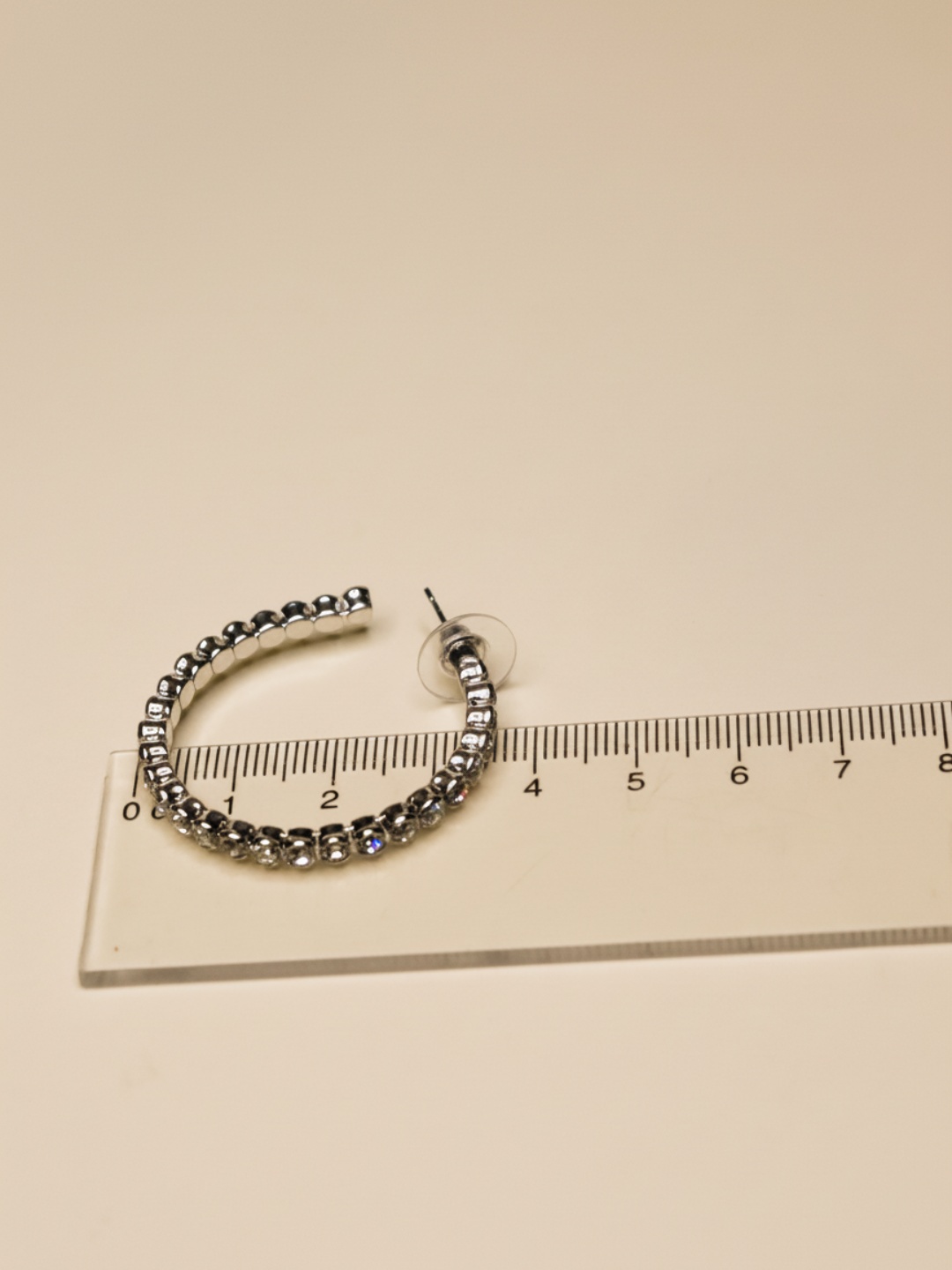 Pendiente de aro plateado con strass junto a una regla — pendientes dorados, primer plano · Lola y Sol (EAR-090)