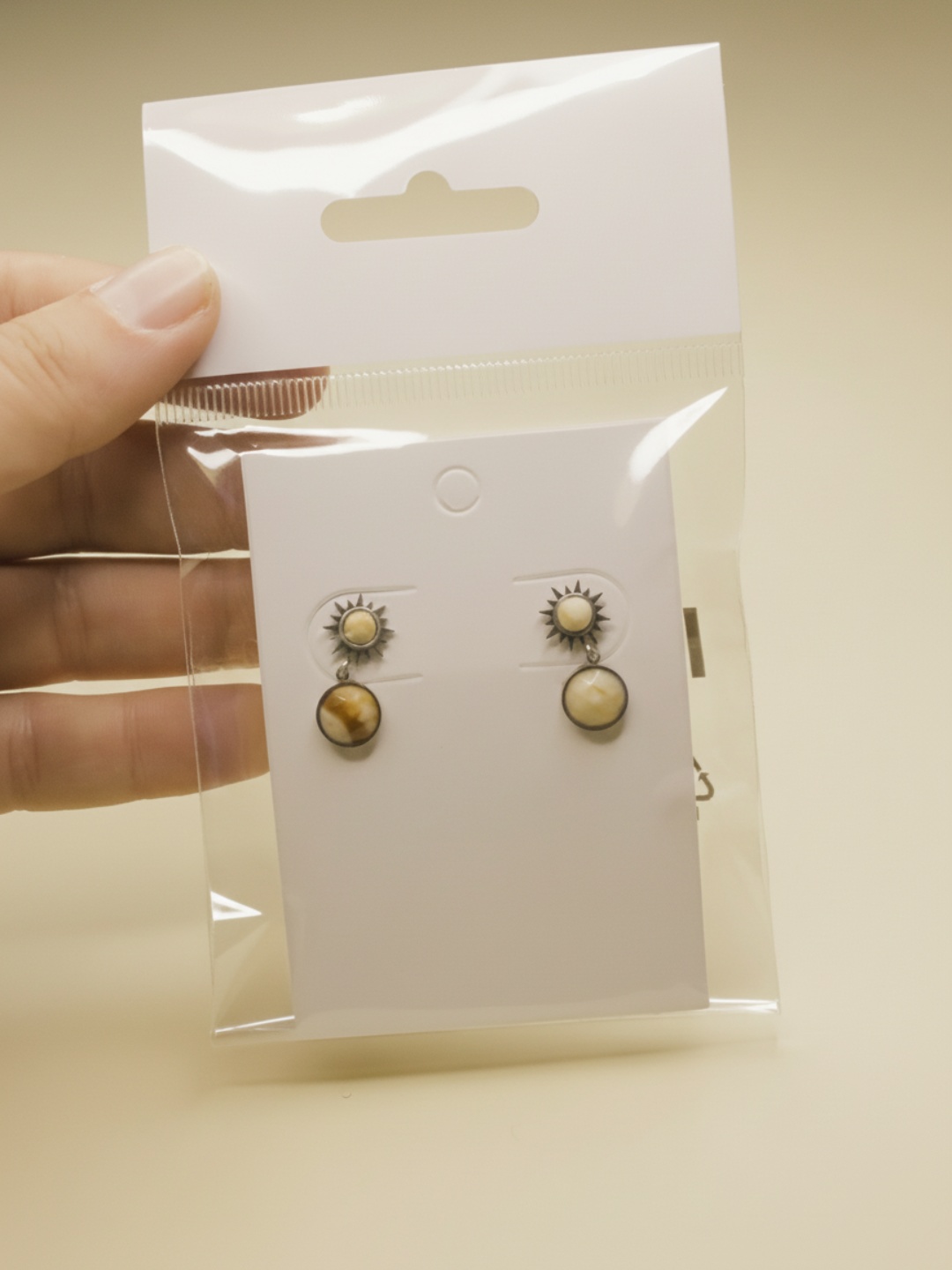 Pendientes colgantes de sol sobre tarjeta blanca en envoltorio transparente — pendientes dorados, primer plano · Lola y Sol (EAR-093)
