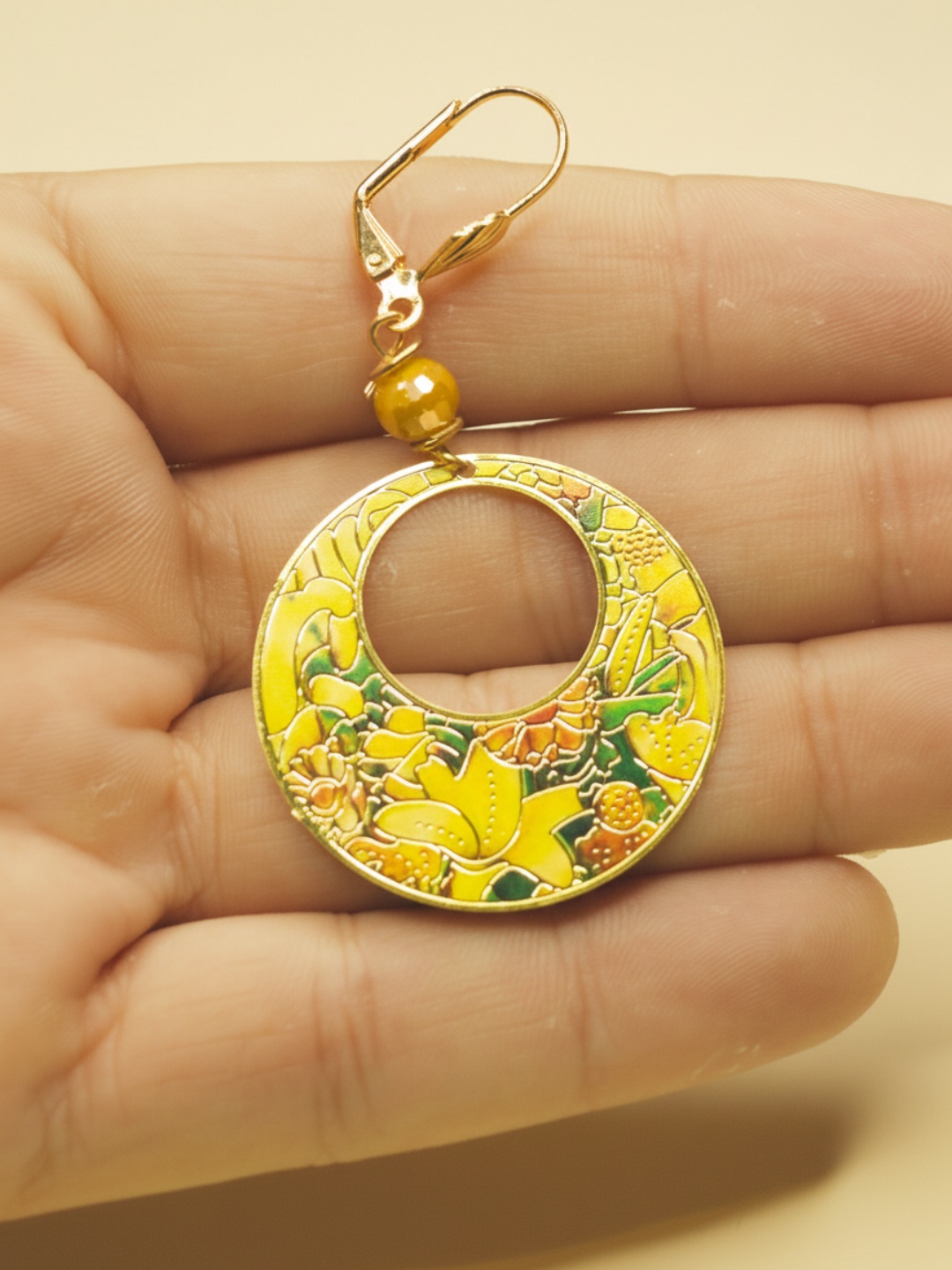 Detalle del colgante circular floral sobre una mano — pendientes baratos, detalle · Lola y Sol (EAR-094)