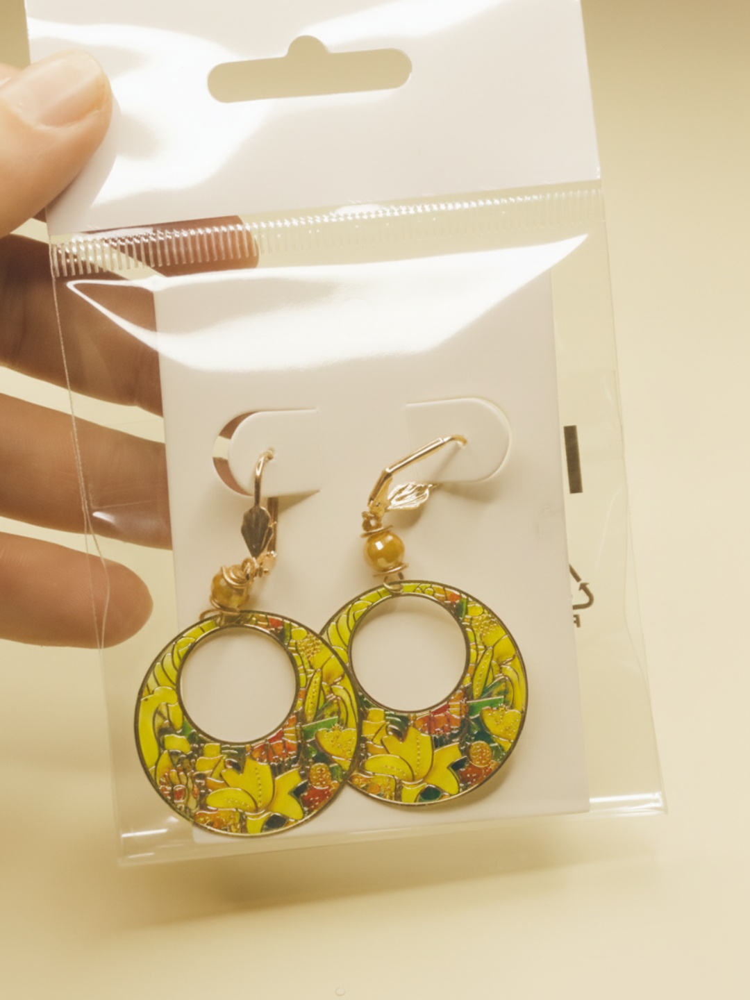 Pendientes florales amarillos sobre tarjeta blanca en envoltorio transparente — pendientes dorados, primer plano · Lola y Sol (EAR-094)