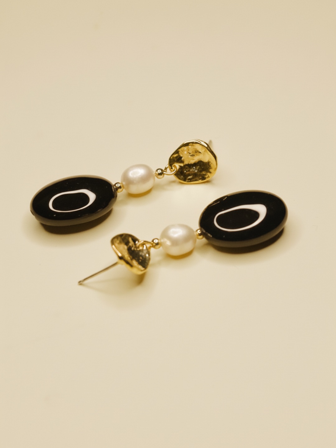 Pendientes colgantes ovalados negros con cuentas nacaradas sobre fondo crema — pendientes para mujer, puestos en la oreja · Lola y Sol (EAR-099)