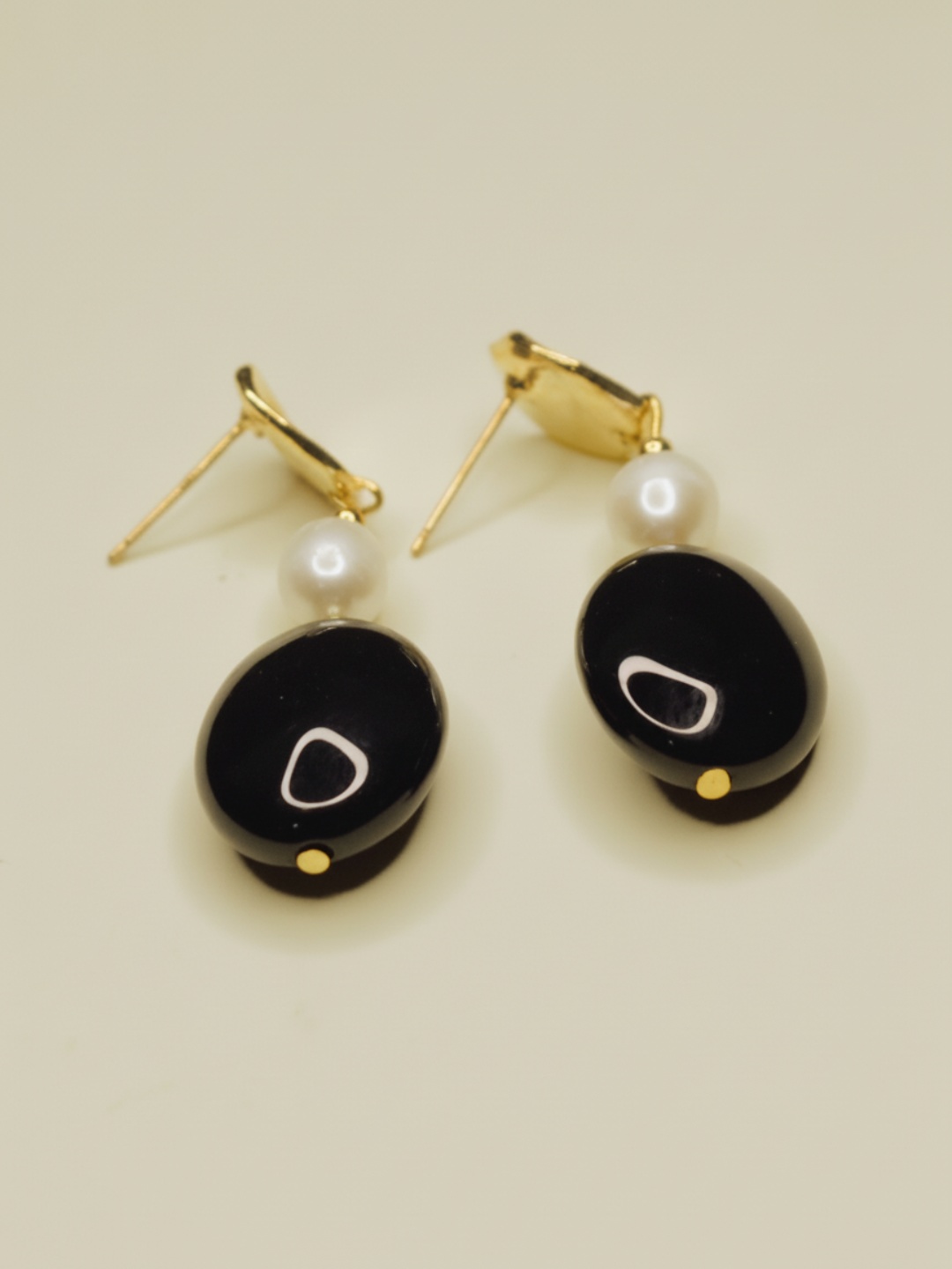Vista inclinada de pendientes negros con pernos dorados visibles — pendientes baratos, puestos en la oreja · Lola y Sol (EAR-099)