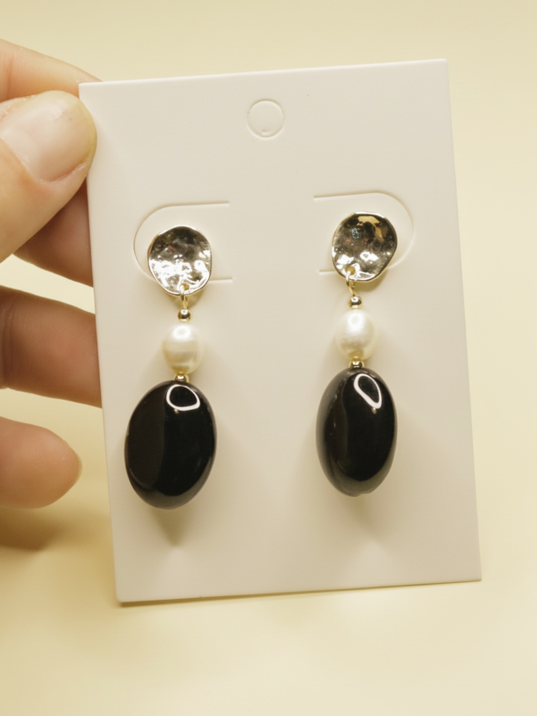 Pendientes negros con detalles nacarados sobre tarjeta blanca — pendientes dorados, puestos en la oreja · Lola y Sol (EAR-099)