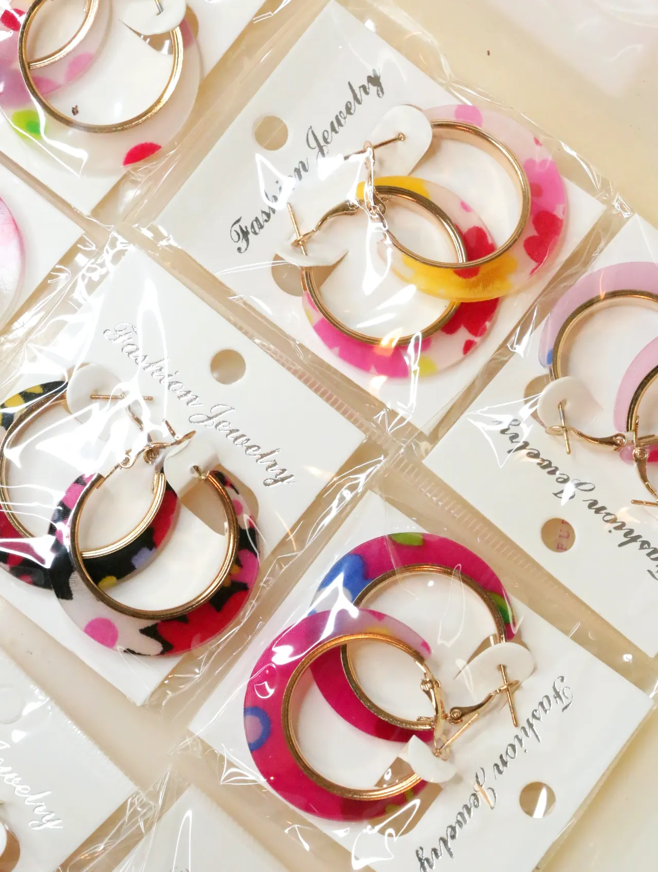 Aros florales multicolor sobre tarjetas blancas — lote de bisutería dorados, primer plano · Lola y Sol (H0008)