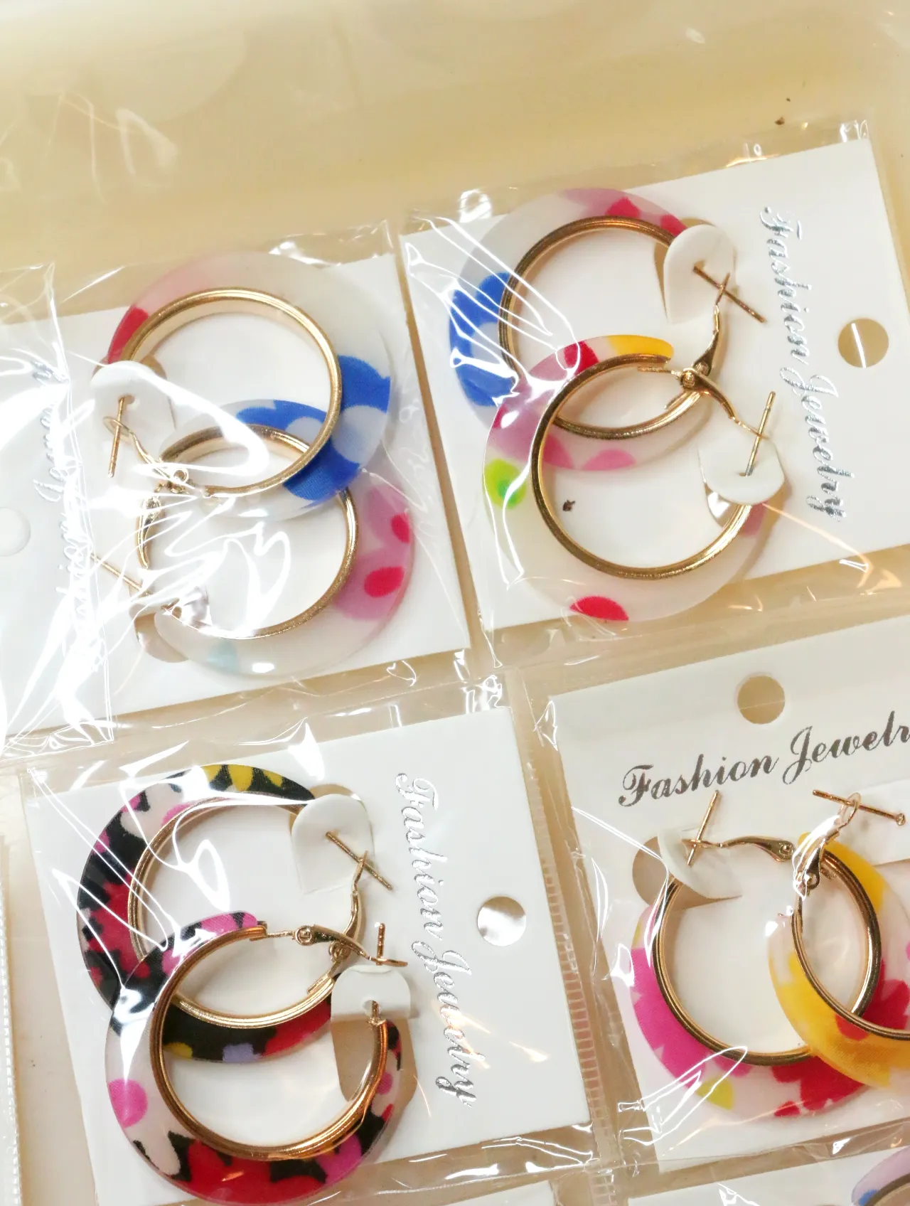 Pendientes de aro con flores en envoltorios transparentes — lote de bisutería de moda, vista lateral · Lola y Sol (H0008)