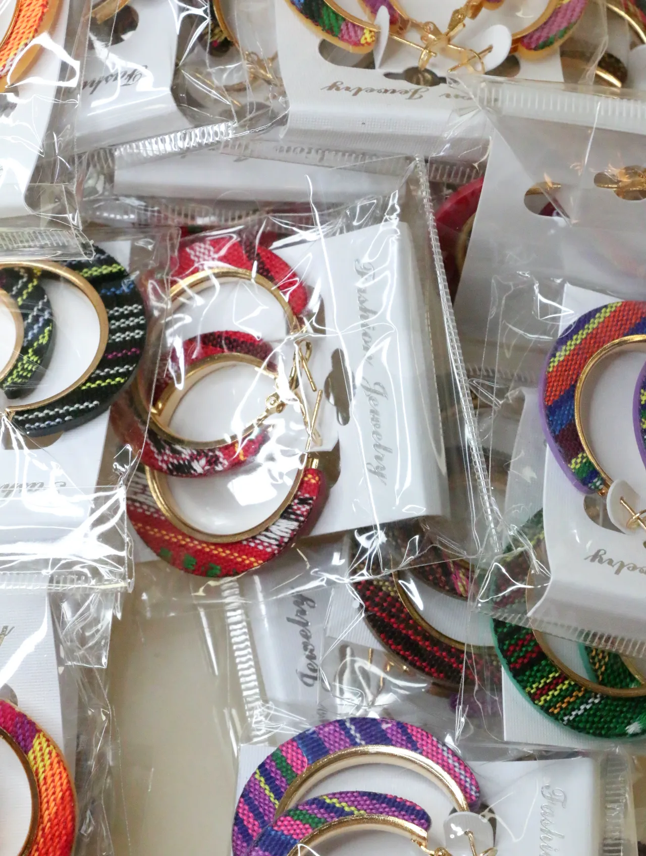Aros en tono dorado con tejido multicolor envasados — lote de bisutería baratos, detalle · Lola y Sol (H0010)