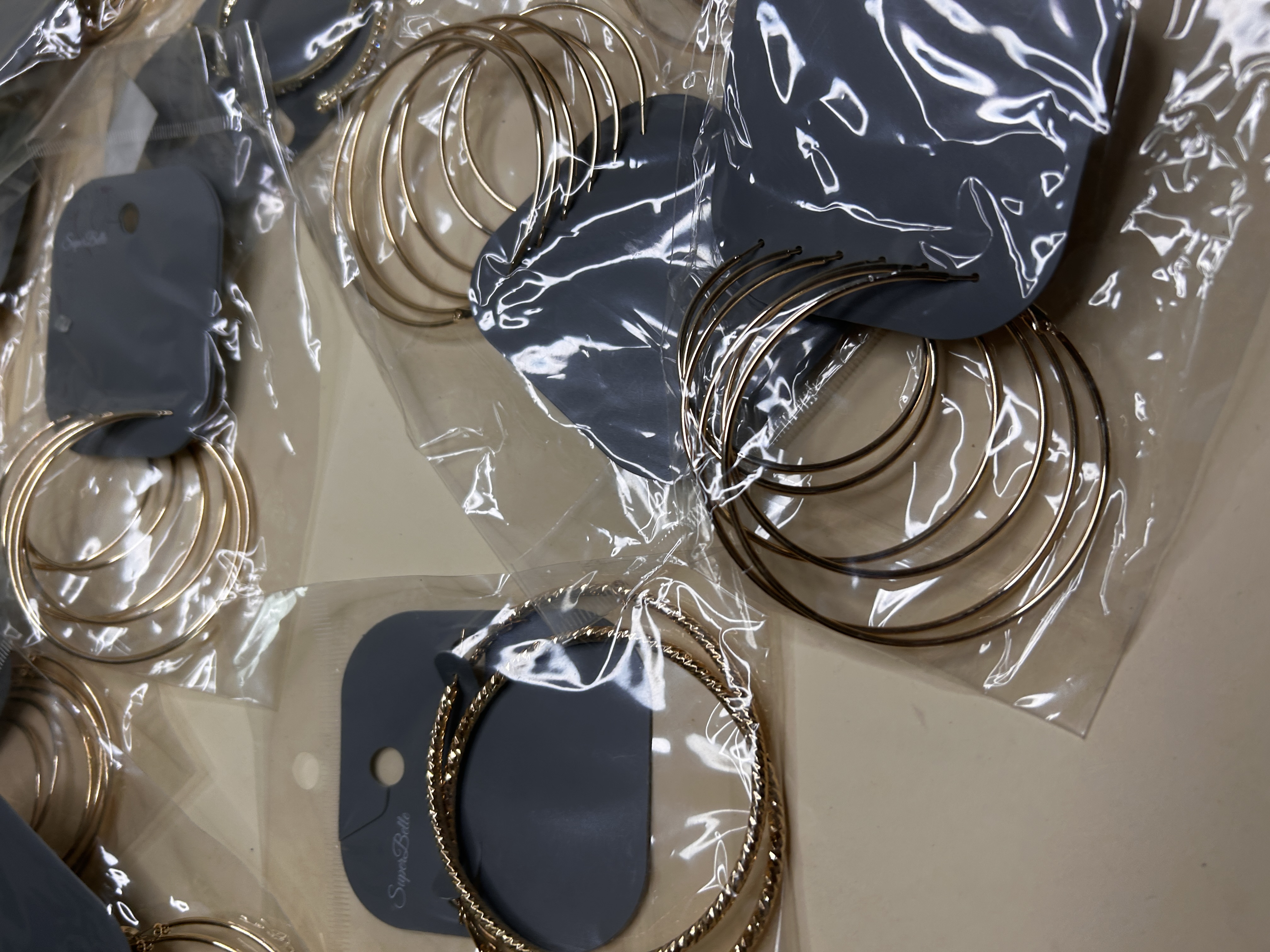 Detalle de aros dorados lisos y trenzados en fundas transparentes — lote de pendientes originales, detalle del acabado · Lola y Sol (HOOP-203)