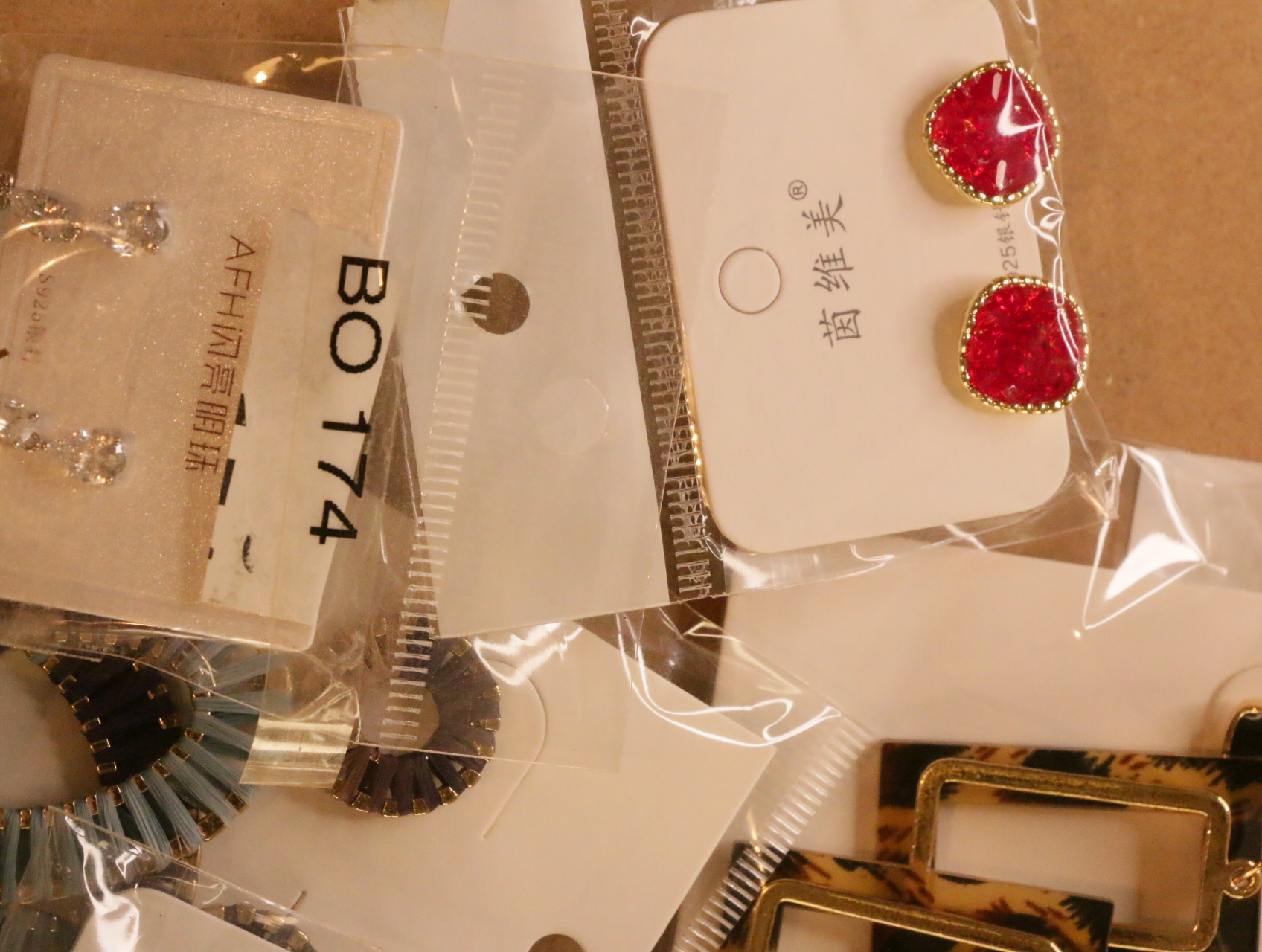 Pendientes de botón rojos junto a diseños brillantes y texturizados — lote de bisutería dorados, primer plano · Lola y Sol (LT039)