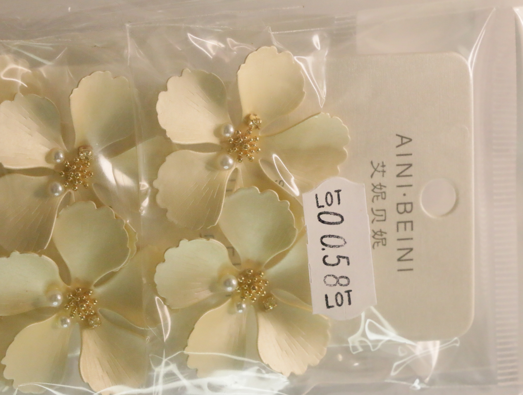 Pendientes de flores crema con etiqueta de referencia interna — lote de bisutería dorados, primer plano · Lola y Sol (LT058)