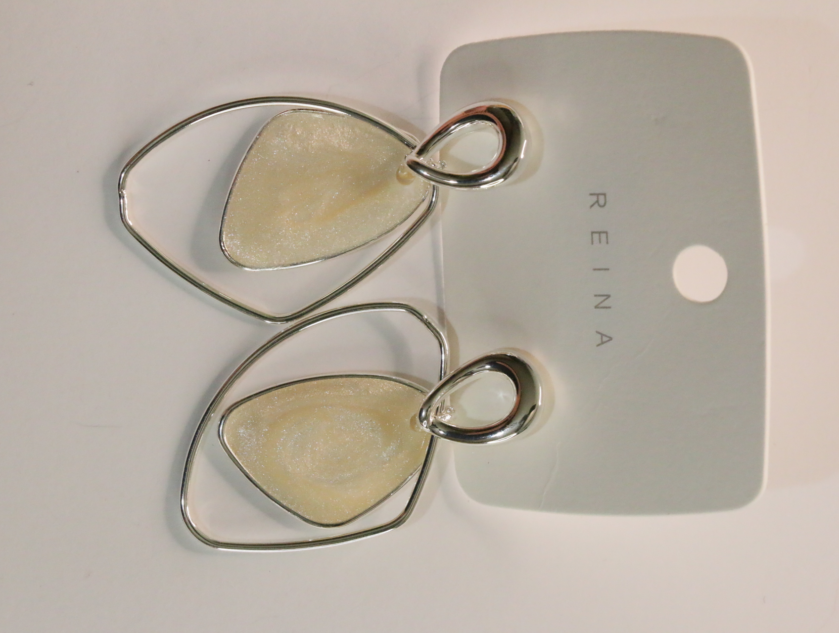 Pendientes geométricos nacarados crema sobre tarjeta REINA — lote de bisutería dorados, primer plano · Lola y Sol (LT059)